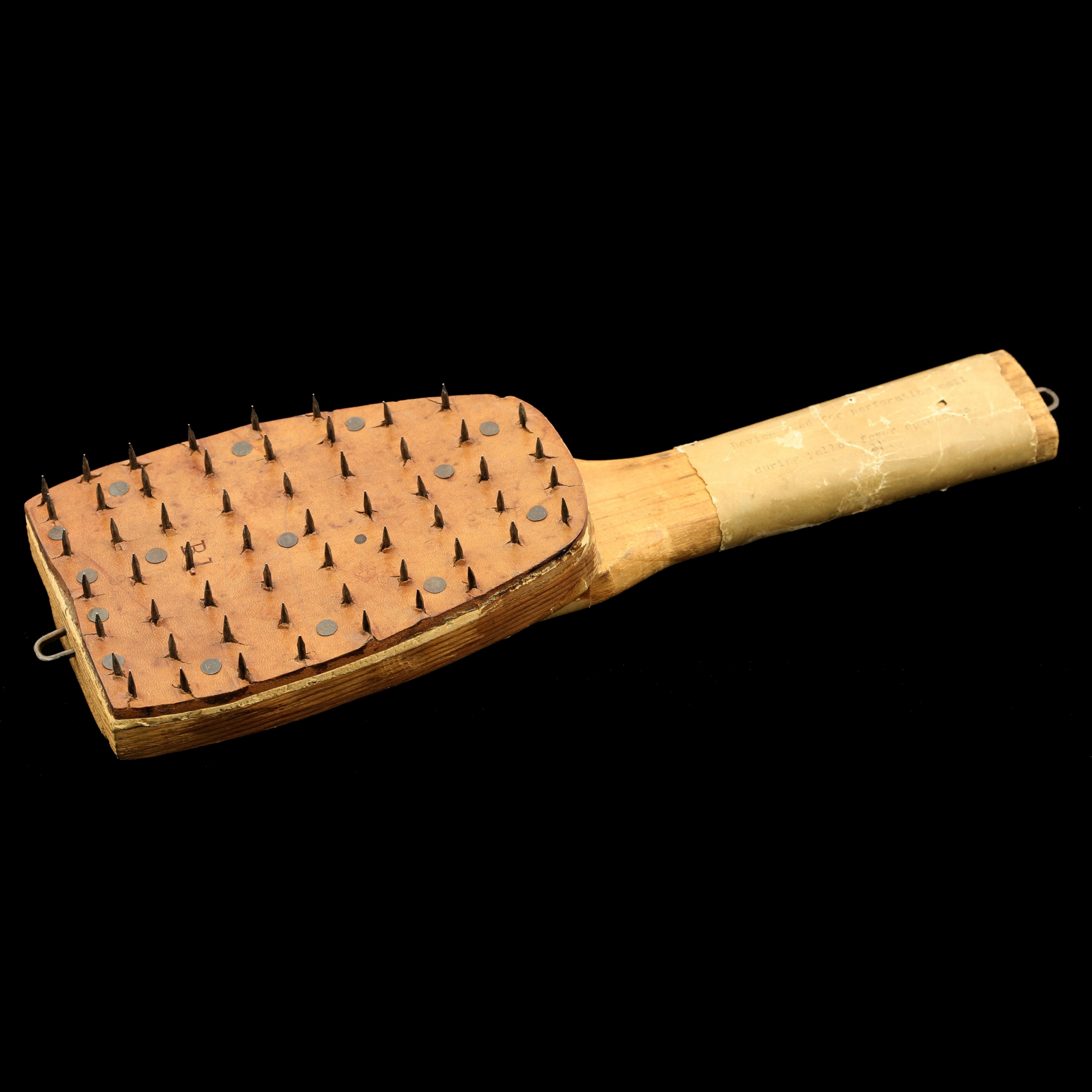 Wooden paddle with nails sticking out of its face.