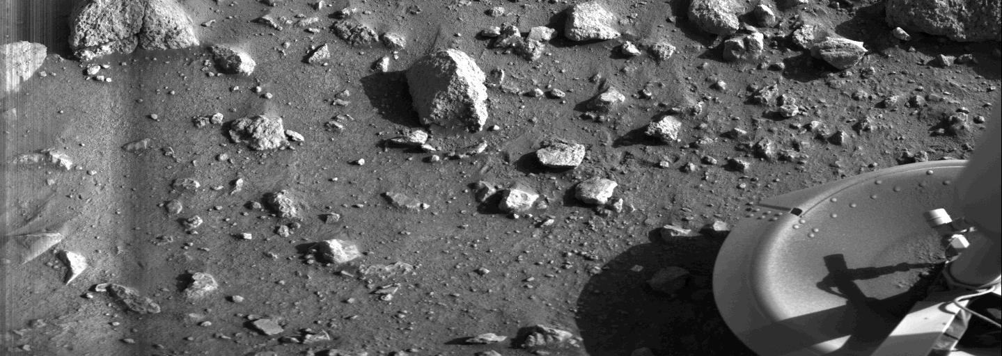 Black and white image of rocks on planet surface with part of a satellite on the right side.