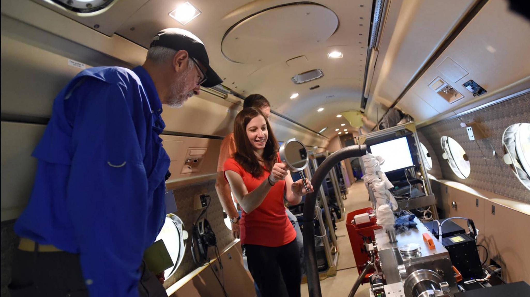 A woman holding a mirror among other people, all inside a plane.