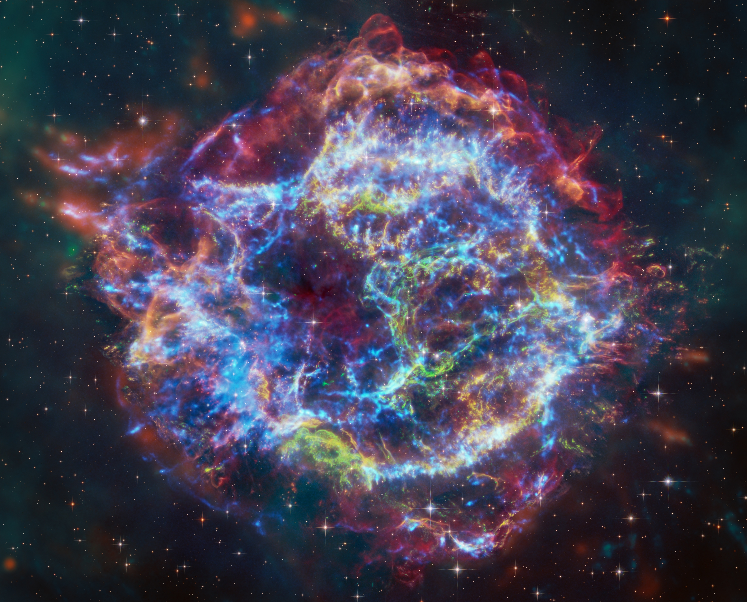 This image of Cassiopeia A resembles a disk of electric light with red clouds, glowing white streaks, red and orange flames, and an area near the center of the remnant resembling a somewhat circular region of green lightning.