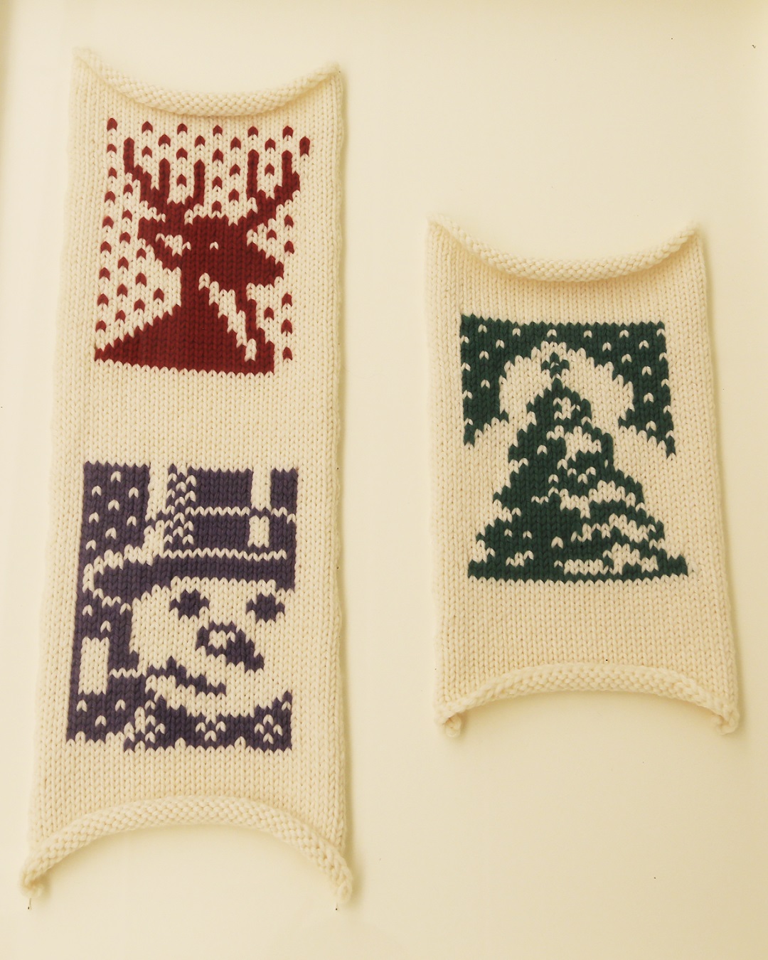 Three knit designs of a red deer, a green tree and a blue snowman