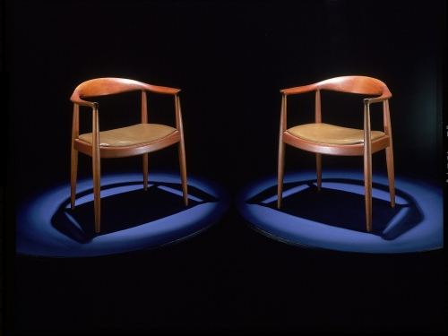 Two teak mid-century modern chairs sit on a black background.