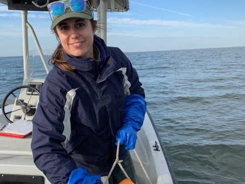 A young woman stoops over the edge of a boat, holding a rectangular rig of PVC pipes with small cameras attached to both sides.