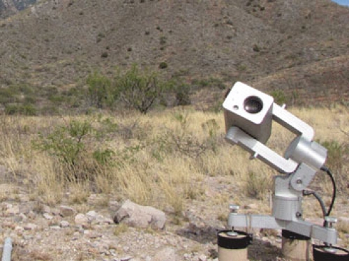 A white telescope in the corner of a photograph with brown hills in the background.