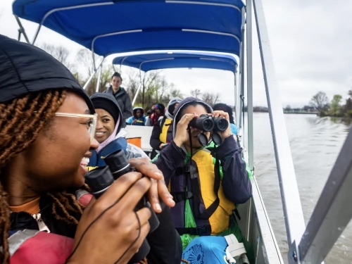 A group of young people on a boat looking into binoculars.