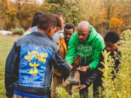 Man in green sweatshirt looking at garden with younger men.