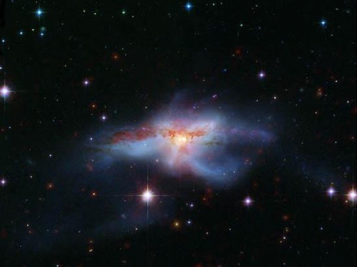 Black sky with red, blue, and white colliding galaxies surrounded by white stars.