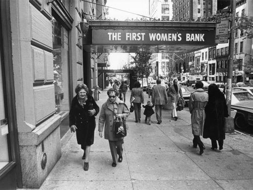 Women walk down the street under the banner of a bank.