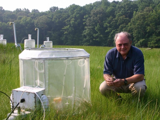 A man kneeling next to a clear contraption that sits over grass. 