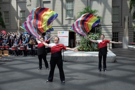 Group of three people in matching outfits wearing rainbow Pride flags.